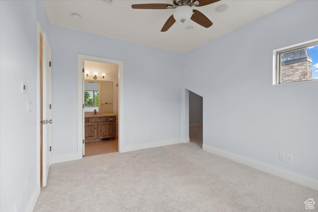 Unfurnished bedroom with light carpet, ensuite bathroom, and a ceiling fan