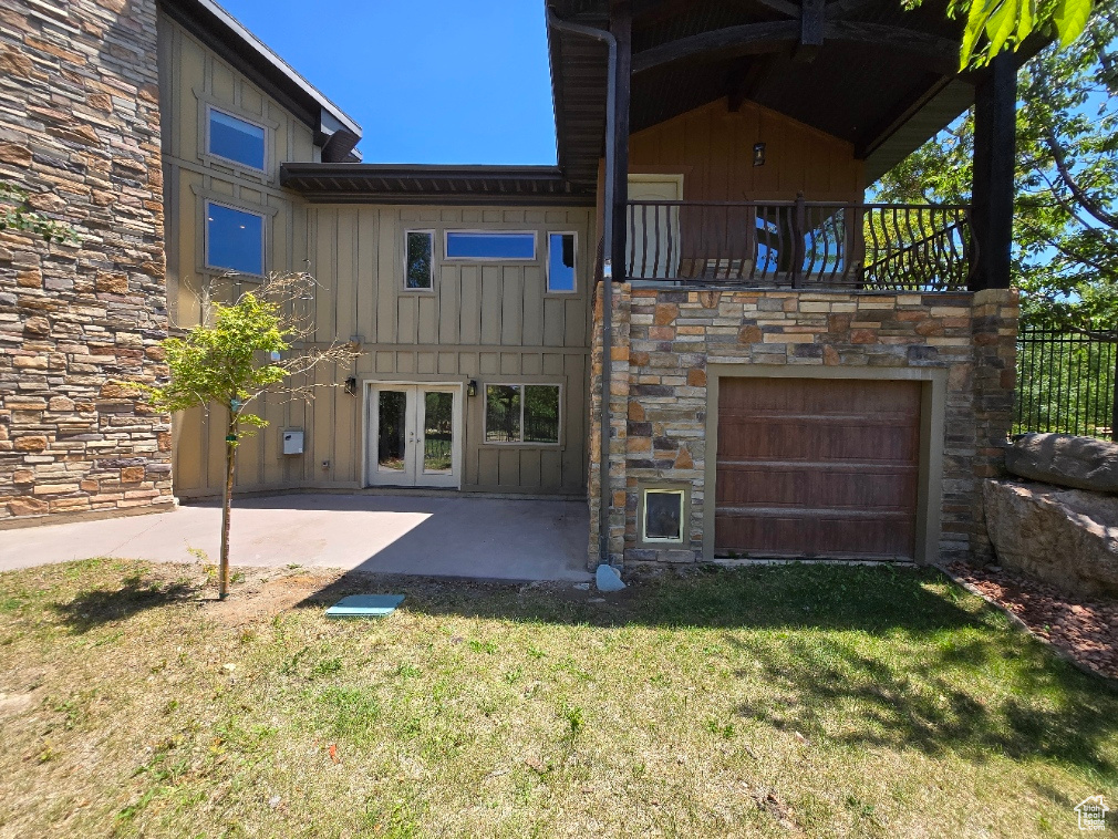 Rear view of house featuring board and batten siding, stone siding, a lawn, a garage, and a patio area