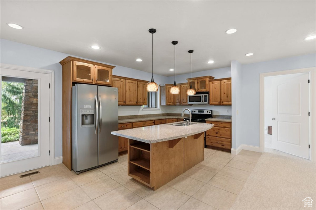 Kitchen with appliances with stainless steel finishes, brown cabinetry, open shelves, an island with sink, and decorative light fixtures