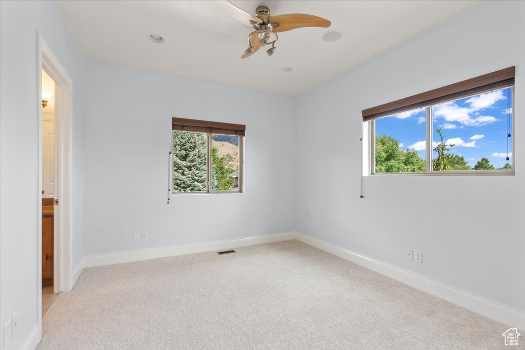 Unfurnished room featuring healthy amount of natural light, light carpet, and a ceiling fan