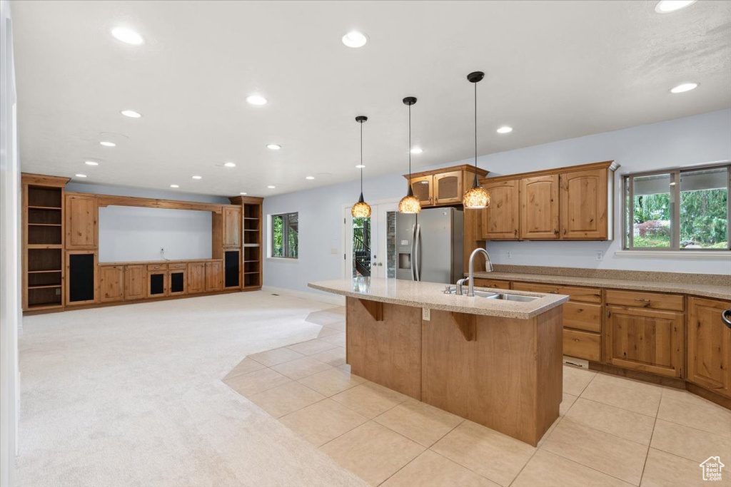 Kitchen featuring stainless steel fridge, light carpet, recessed lighting, a breakfast bar, and a center island with sink