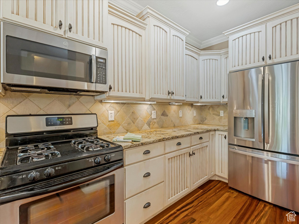 Kitchen featuring appliances with stainless steel finishes, crown molding, cream cabinets, dark wood-style flooring, and light stone countertops