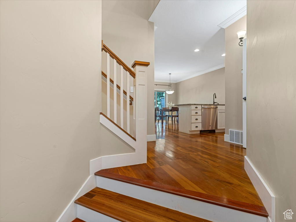Staircase with ornamental molding, wood finished floors, and recessed lighting
