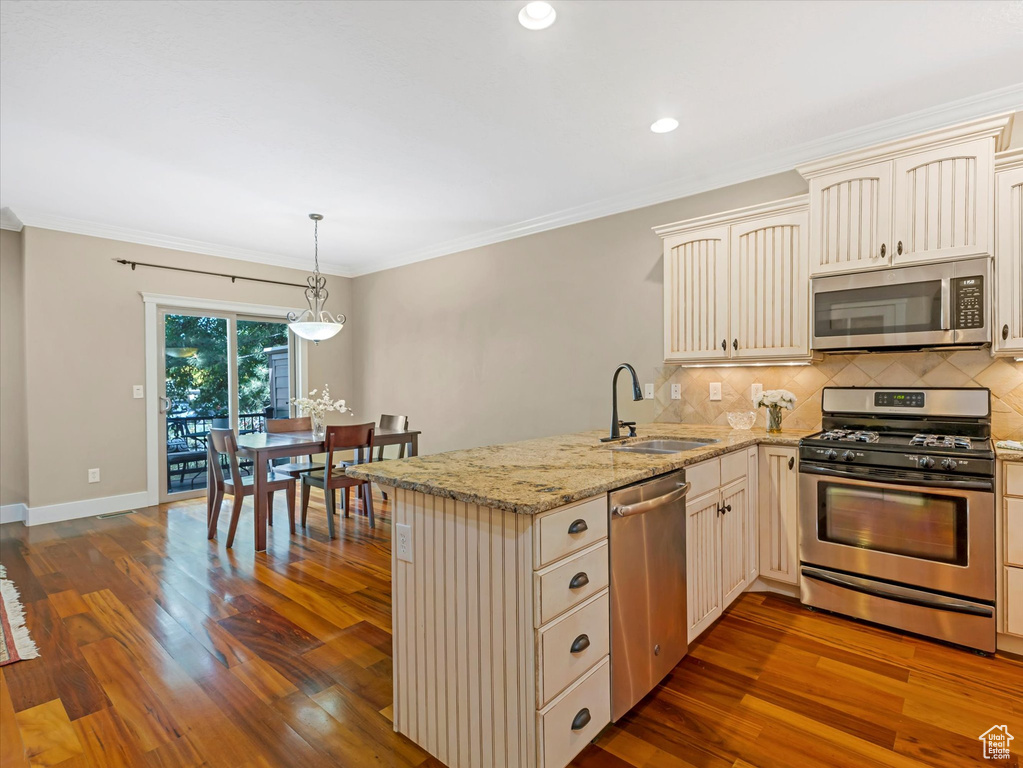 Kitchen featuring stainless steel appliances, cream cabinets, a peninsula, tasteful backsplash, and dark wood-style floors