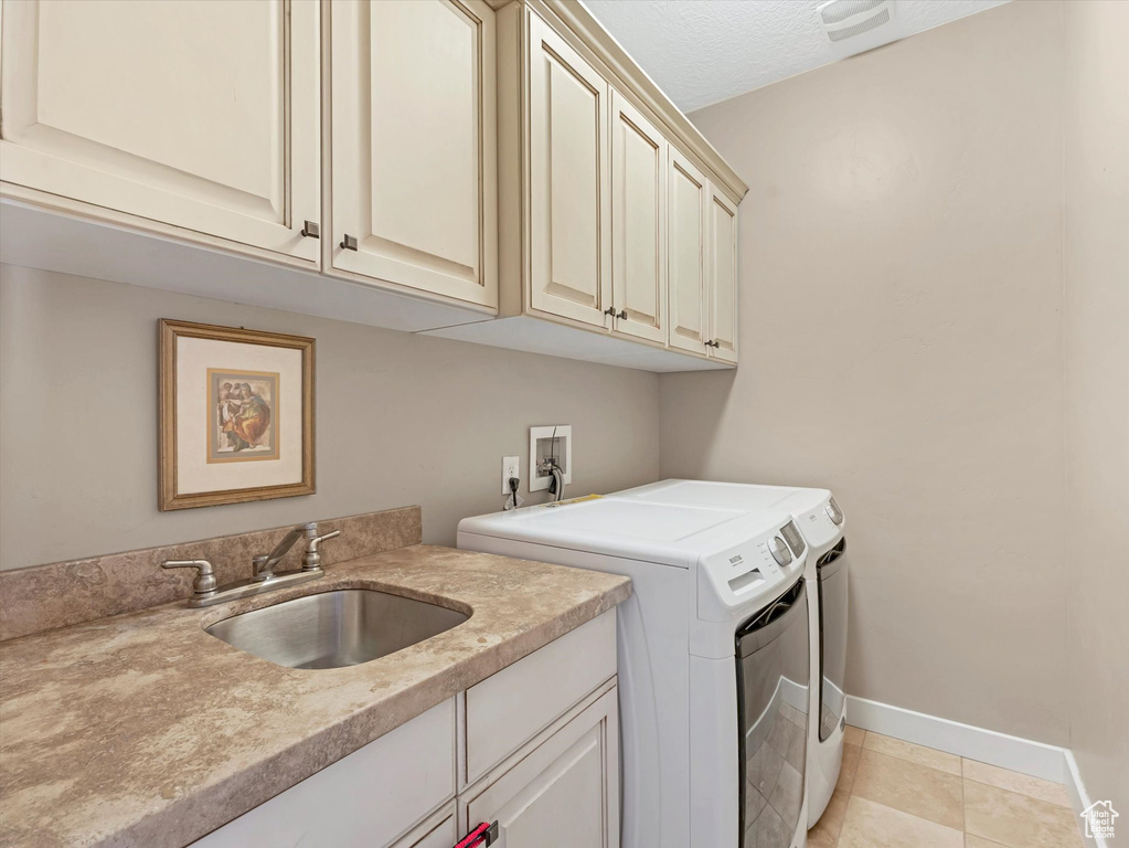 Washroom featuring washer and clothes dryer, cabinet space, and light tile patterned flooring
