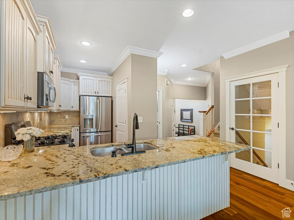 Kitchen with stainless steel appliances, a peninsula, ornamental molding, dark wood-style flooring, and light stone counters