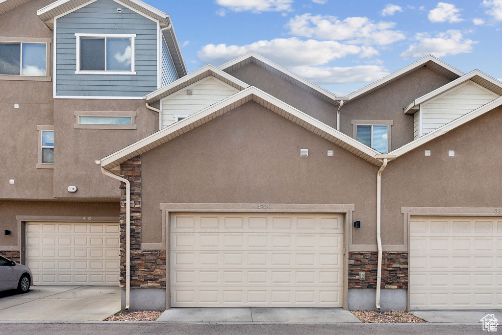 Townhome / multi-family property featuring stone siding, stucco siding, and driveway