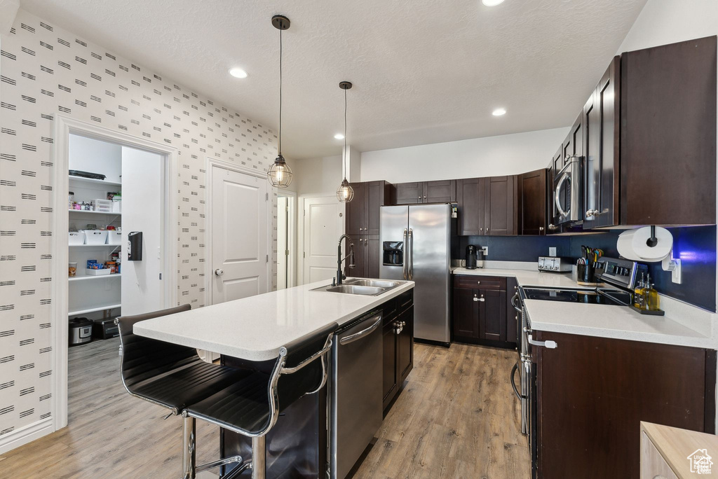 Kitchen with appliances with stainless steel finishes, light wood-style flooring, light countertops, dark brown cabinetry, and wallpapered walls