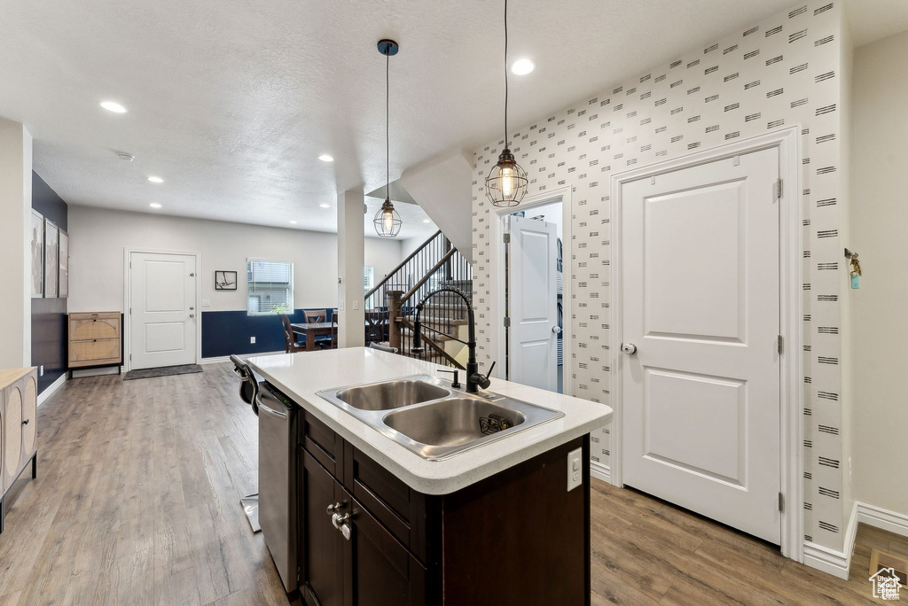 Kitchen featuring stainless steel dishwasher, dark brown cabinetry, light countertops, light wood-style floors, and pendant lighting