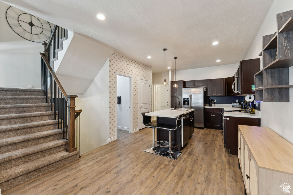 Kitchen with appliances with stainless steel finishes, light countertops, open shelves, dark brown cabinets, and a kitchen island with sink