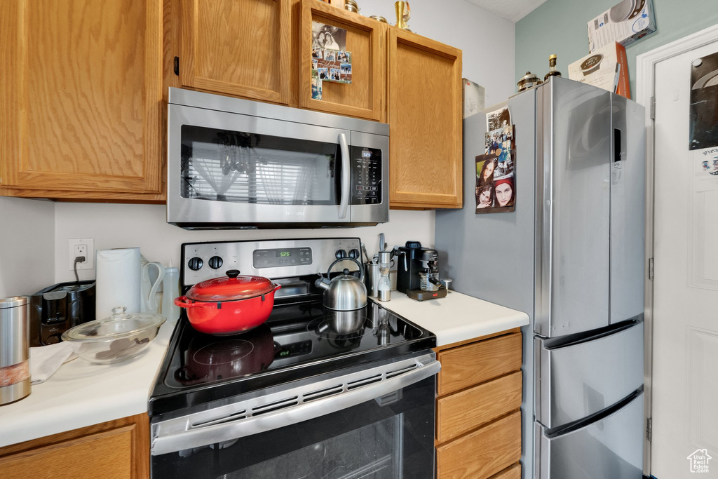Kitchen featuring stainless steel appliances, light countertops, and brown cabinetry
