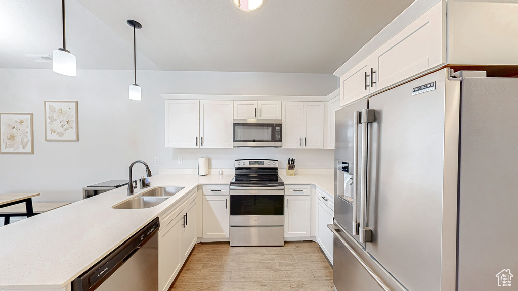 Kitchen featuring appliances with stainless steel finishes, a peninsula, light countertops, light wood finished floors, and white cabinetry