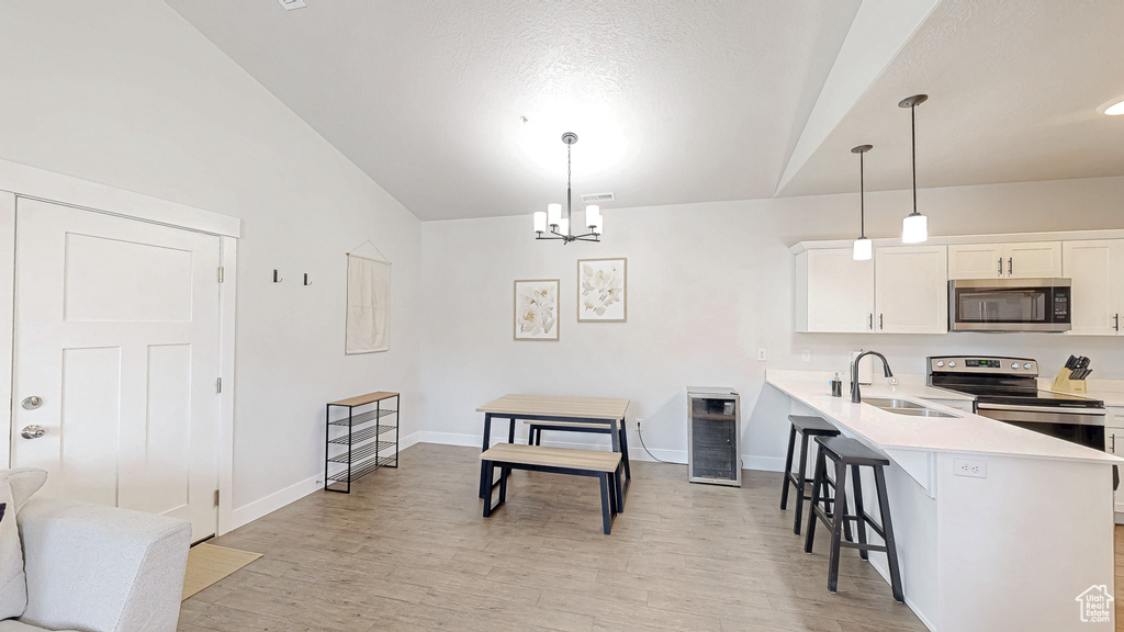 Kitchen with stainless steel appliances, vaulted ceiling, a breakfast bar area, light countertops, and light wood finished floors