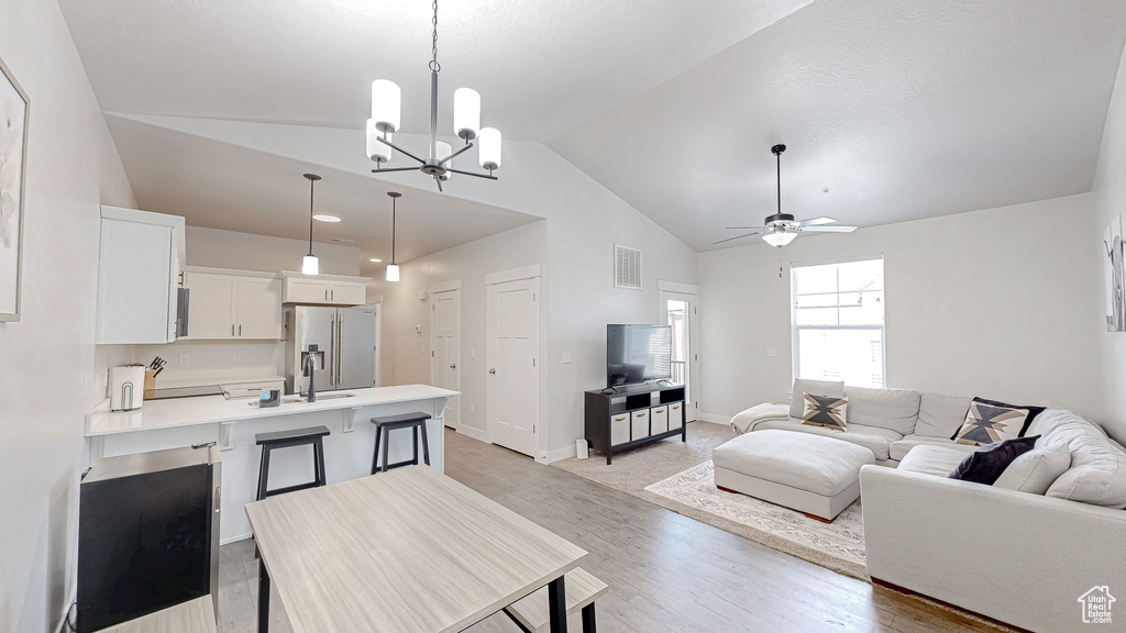 Living room with lofted ceiling, a chandelier, light wood-style flooring, and ceiling fan