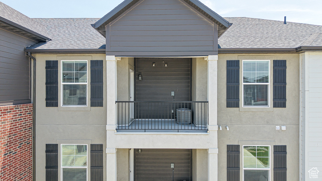 View of front of house with a balcony, a shingled roof, and stucco siding