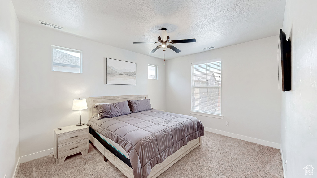 Bedroom featuring a textured ceiling, light colored carpet, and a ceiling fan