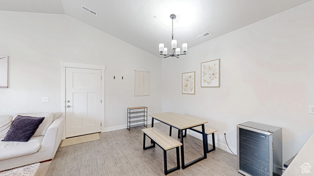 Dining space featuring beverage cooler, a chandelier, vaulted ceiling, and light wood-type flooring