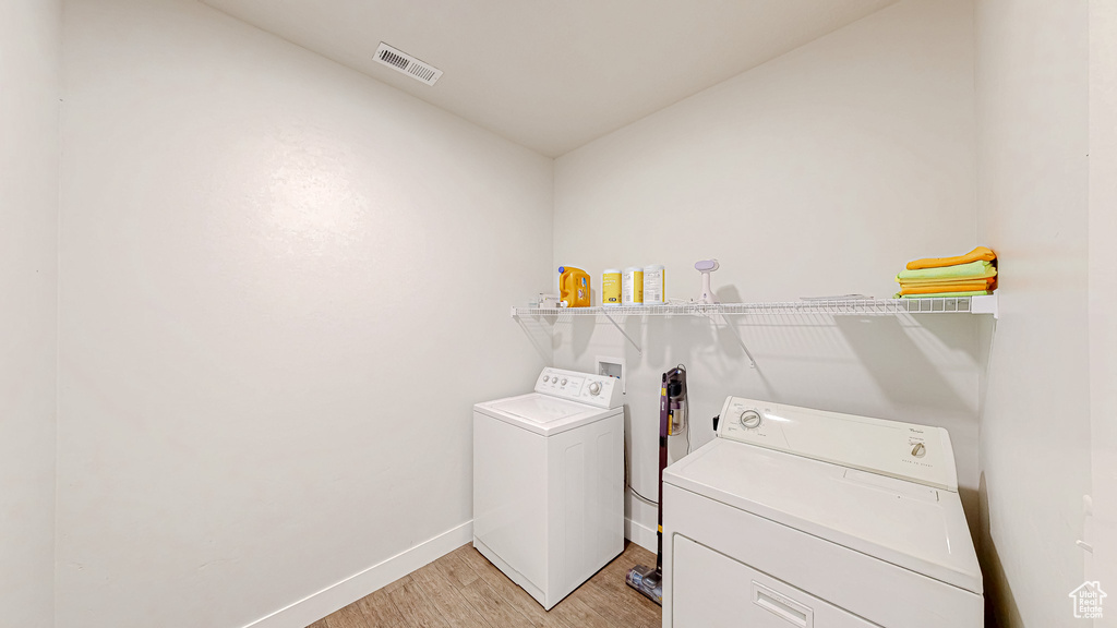 Laundry room with washing machine and clothes dryer and light wood finished floors