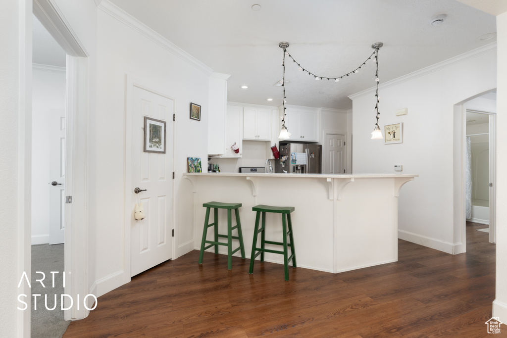 Kitchen featuring freestanding refrigerator, ornamental molding, a breakfast bar area, dark wood-style floors, and light countertops