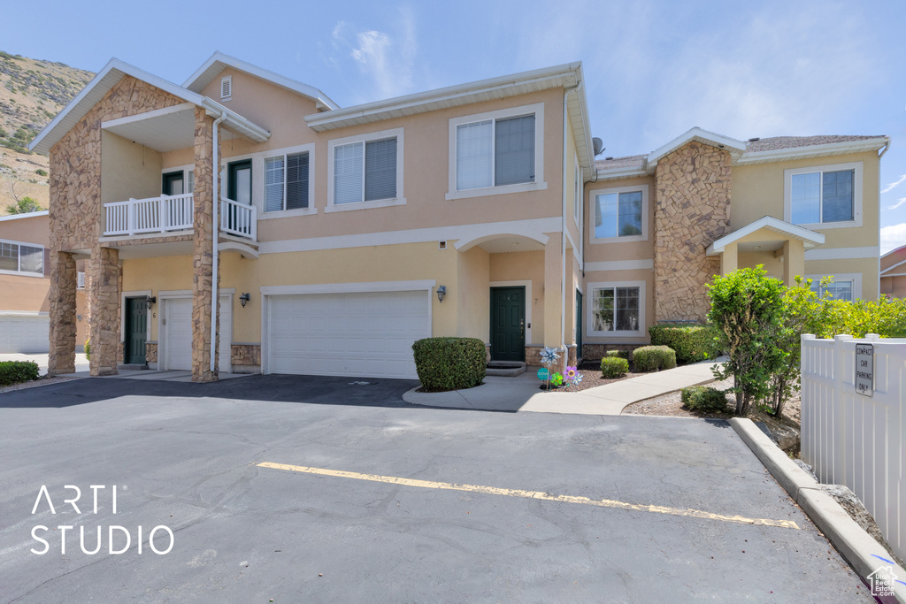 View of property with stucco siding, stone siding, a garage, and driveway