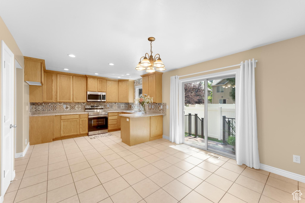 Kitchen featuring appliances with stainless steel finishes, light countertops, backsplash, a chandelier, and a peninsula