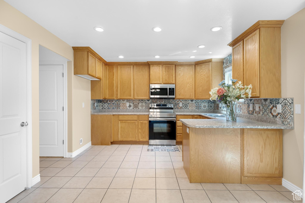 Kitchen with stainless steel appliances, a peninsula, tasteful backsplash, light tile patterned flooring, and recessed lighting