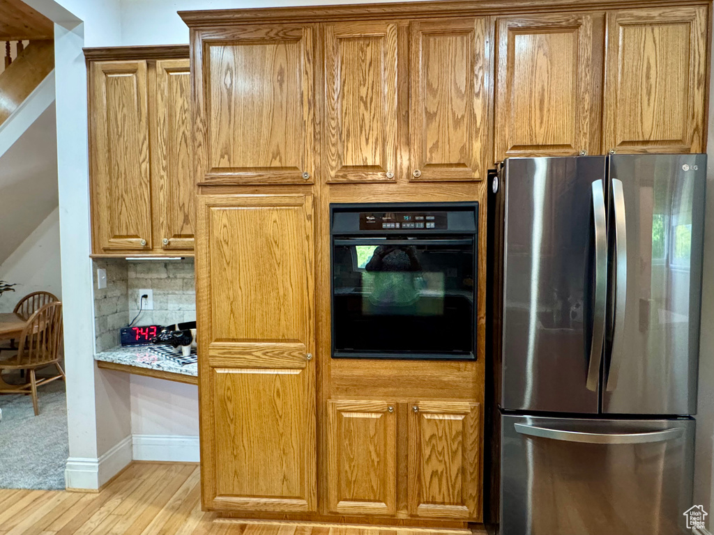 Kitchen with freestanding refrigerator, oven, light wood-style floors, brown cabinetry, and decorative backsplash