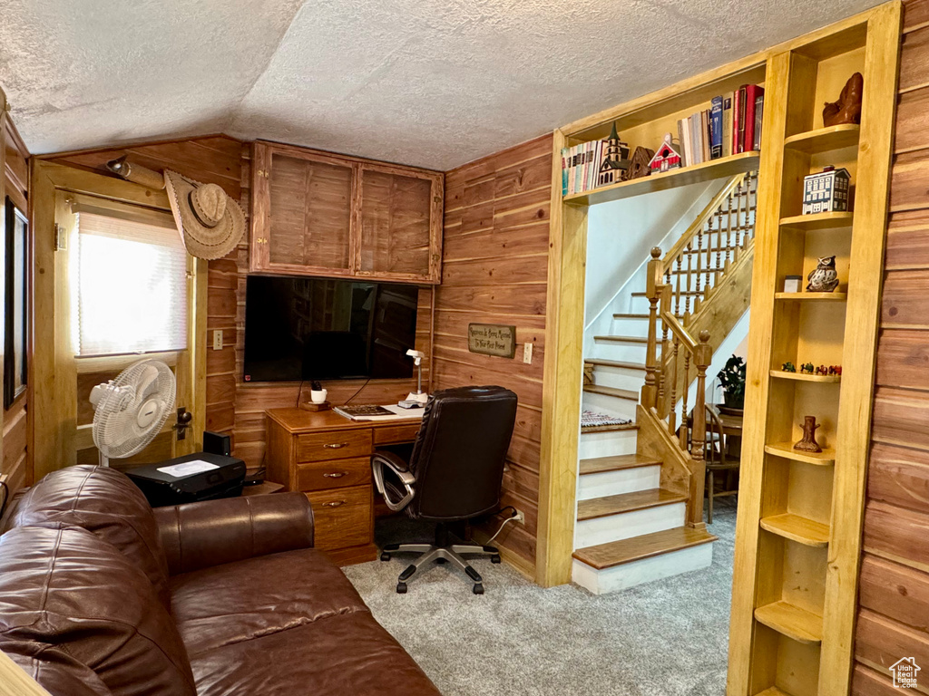 Carpeted office space featuring wooden walls, a textured ceiling, and vaulted ceiling
