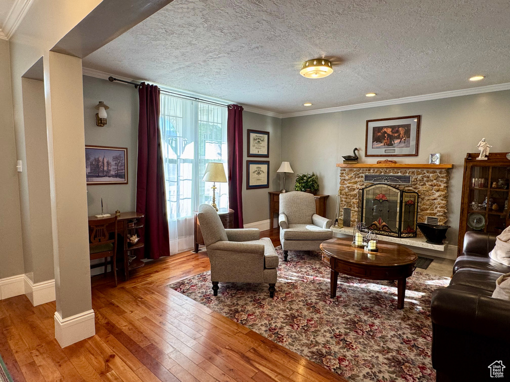 Living area featuring hardwood / wood-style flooring, a fireplace, crown molding, a textured ceiling, and recessed lighting