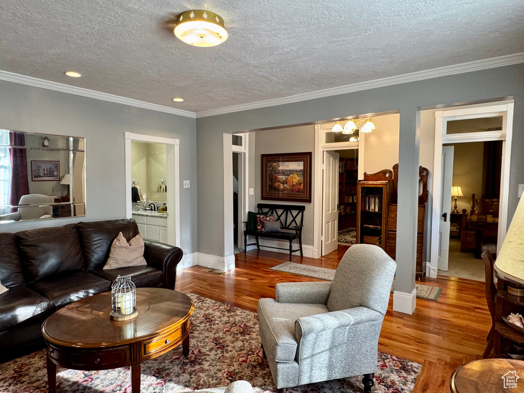 Living area featuring wood finished floors, a textured ceiling, ornamental molding, a chandelier, and recessed lighting