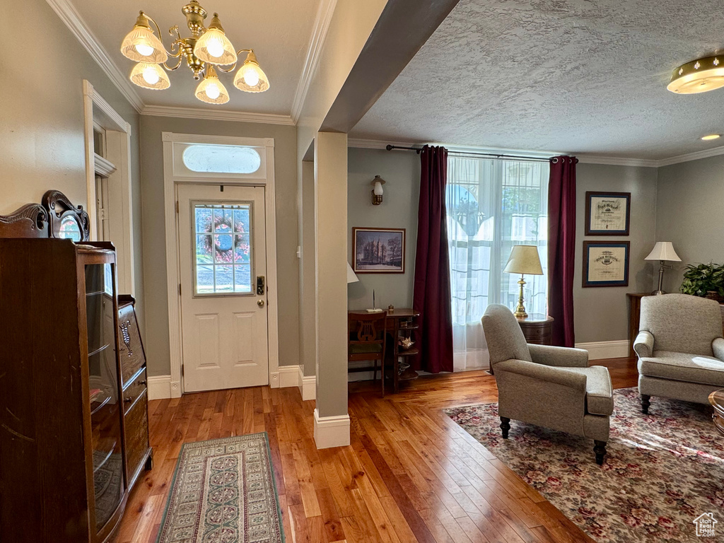 Foyer entrance with plenty of natural light, light wood finished floors, a chandelier, and ornamental molding