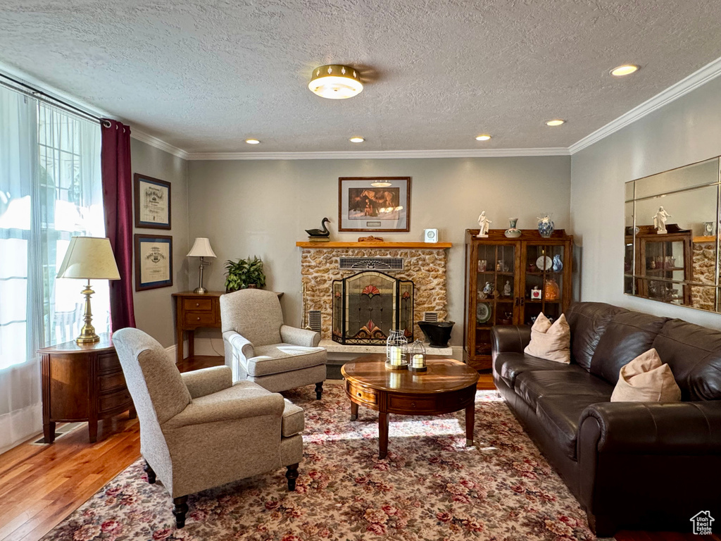 Living room with plenty of natural light, wood finished floors, a stone fireplace, a textured ceiling, and recessed lighting
