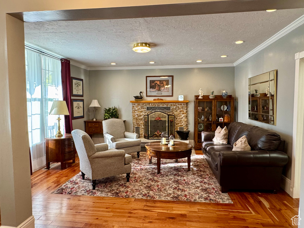 Living area featuring a stone fireplace, hardwood / wood-style flooring, a textured ceiling, crown molding, and recessed lighting