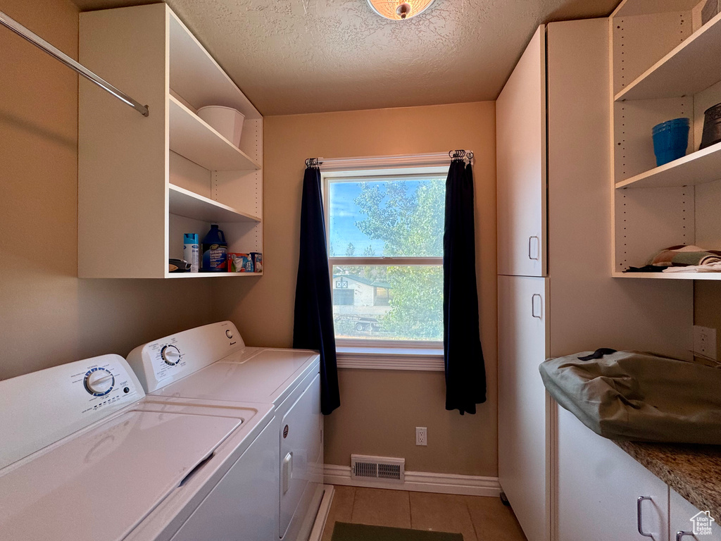 Laundry room featuring independent washer and dryer, cabinet space, light tile patterned floors, and a textured ceiling