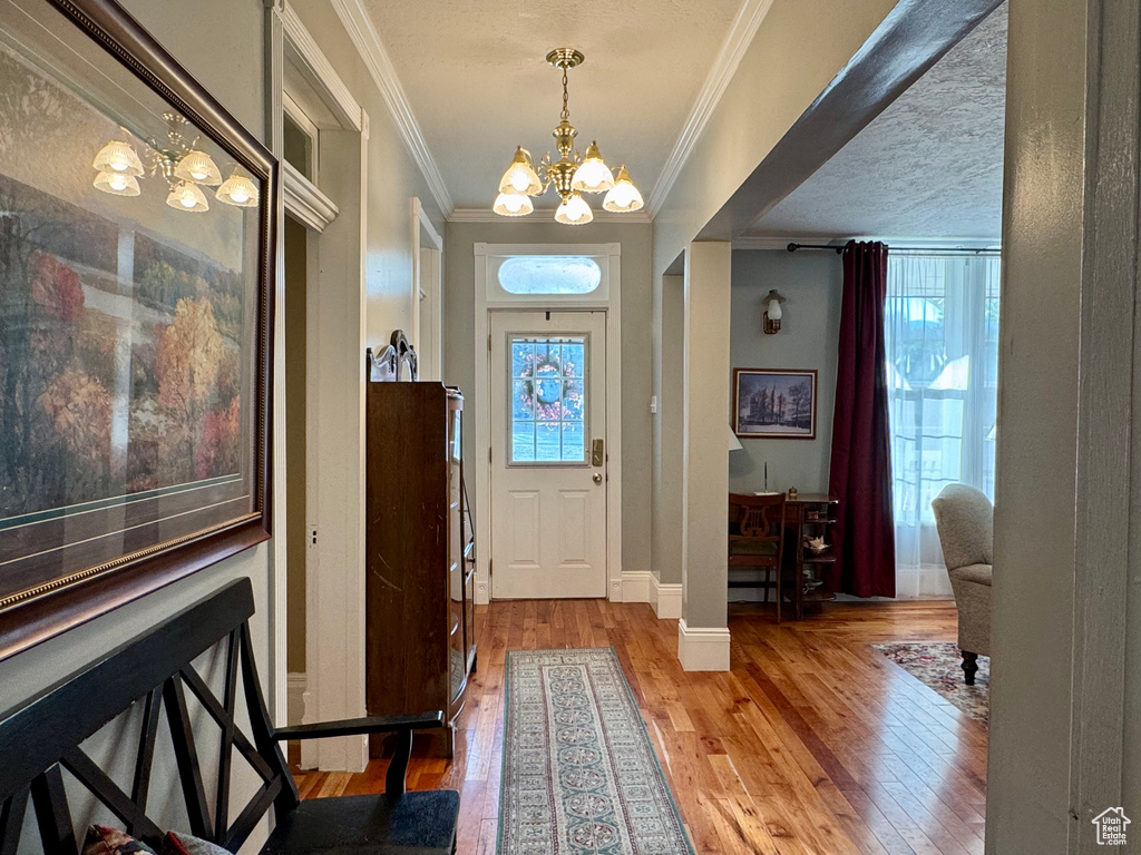 Foyer with a chandelier, crown molding, and light wood-type flooring