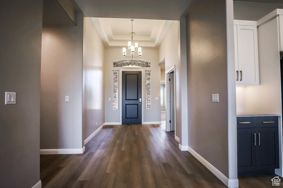 Entryway featuring a raised ceiling, dark wood-type flooring, and a chandelier