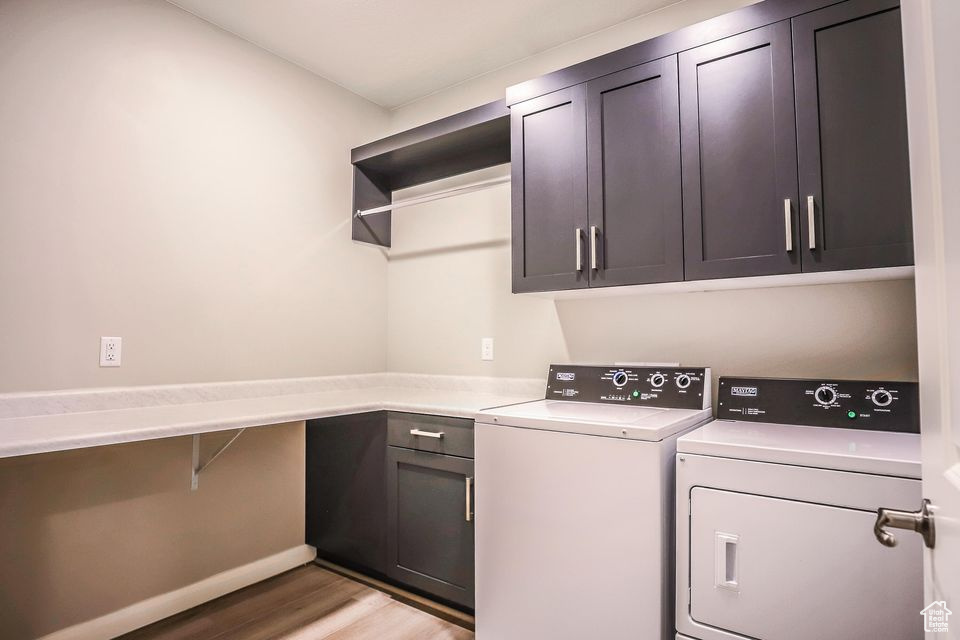 Laundry area with cabinet space, separate washer and dryer, and light wood-style floors