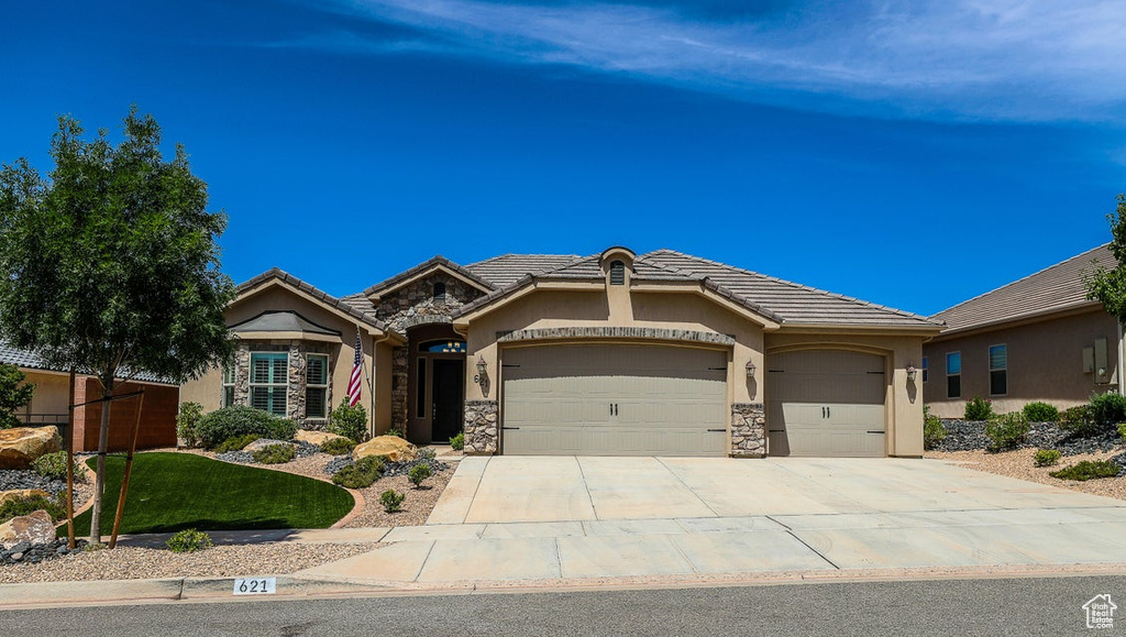 French country style house featuring a garage, stucco siding, driveway, stone siding, and a tiled roof