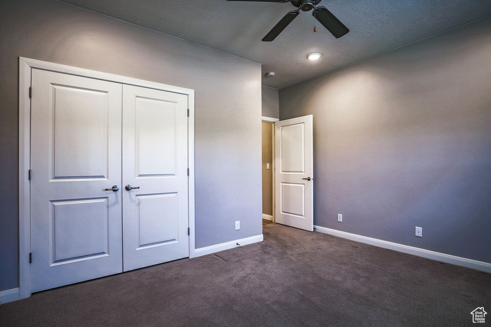 Unfurnished bedroom featuring dark carpet, a closet, and ceiling fan
