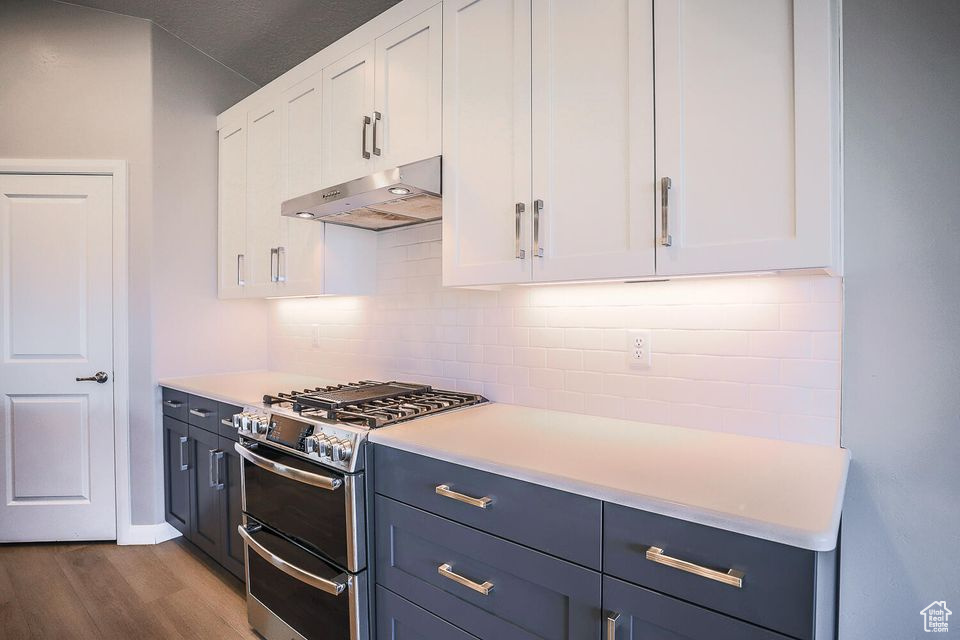 Kitchen featuring under cabinet range hood, double oven range, white cabinets, and tasteful backsplash