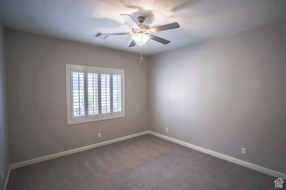 Empty room with ceiling fan, a textured ceiling, and carpet