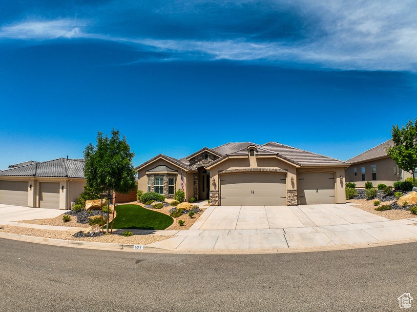 Single story home with stucco siding, a tiled roof, an attached garage, driveway, and stone siding
