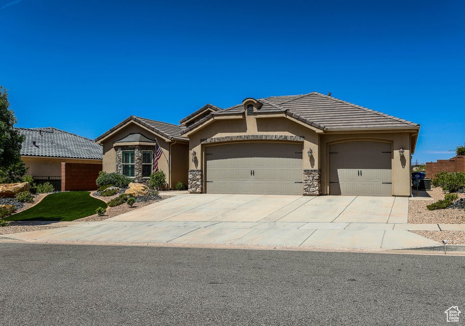 View of front of house featuring a garage, stucco siding, a tile roof, driveway, and stone siding