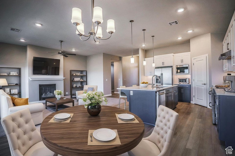 Dining space featuring ceiling fan, dark wood finished floors, a chandelier, a glass covered fireplace, and recessed lighting