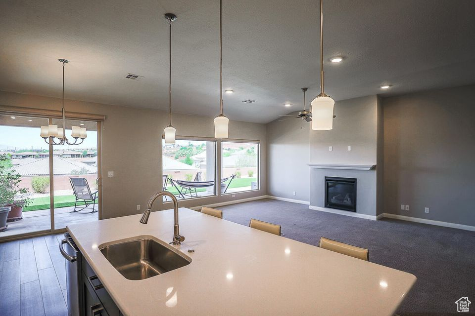 Kitchen featuring a ceiling fan, light countertops, an island with sink, a glass covered fireplace, and a chandelier