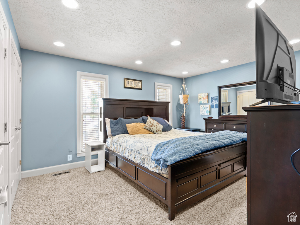 Bedroom with light carpet, a textured ceiling, and recessed lighting