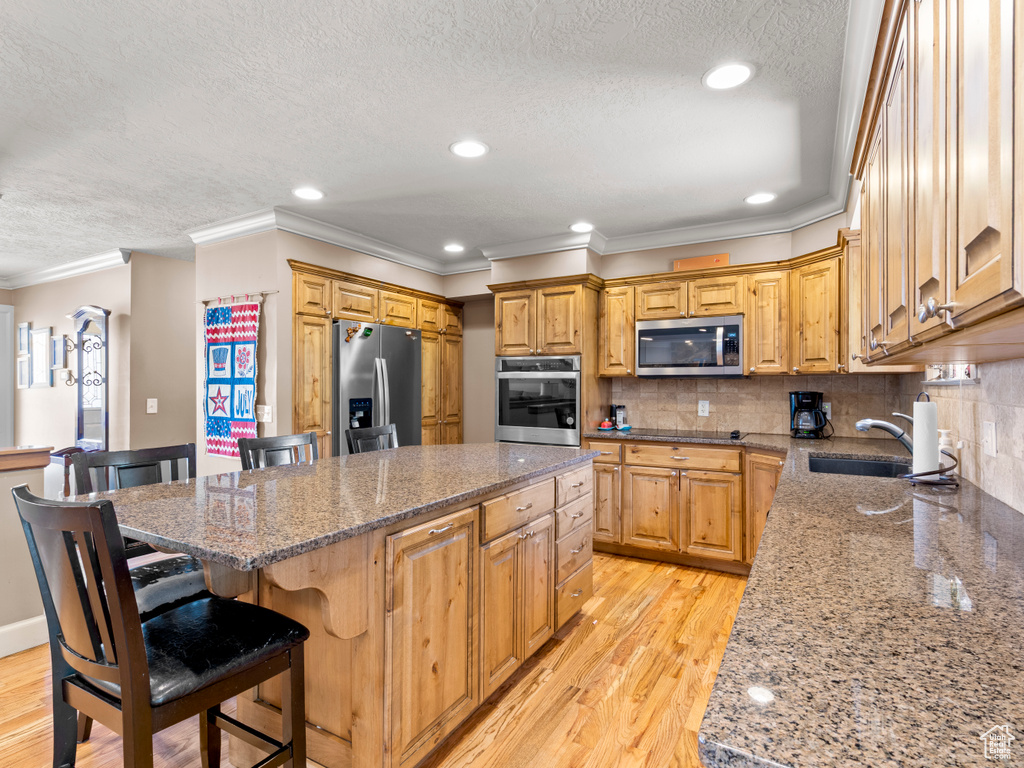 Kitchen with appliances with stainless steel finishes, a textured ceiling, a center island, ornamental molding, and a kitchen breakfast bar