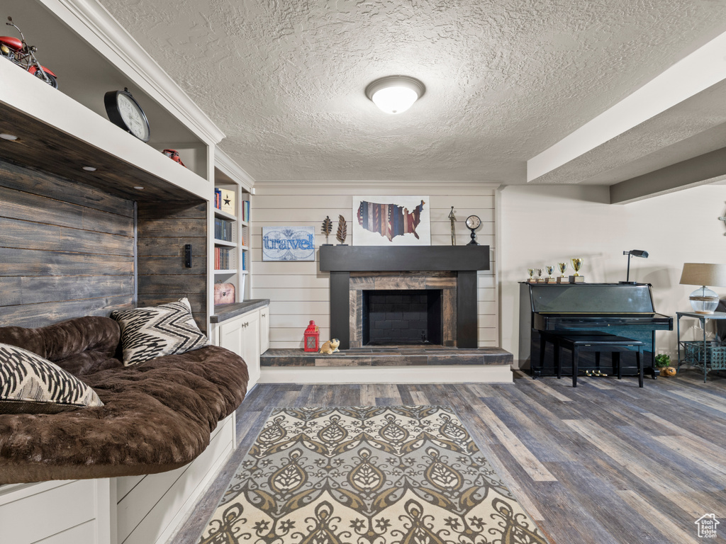 Living area featuring a textured ceiling, wood finished floors, and a fireplace with raised hearth