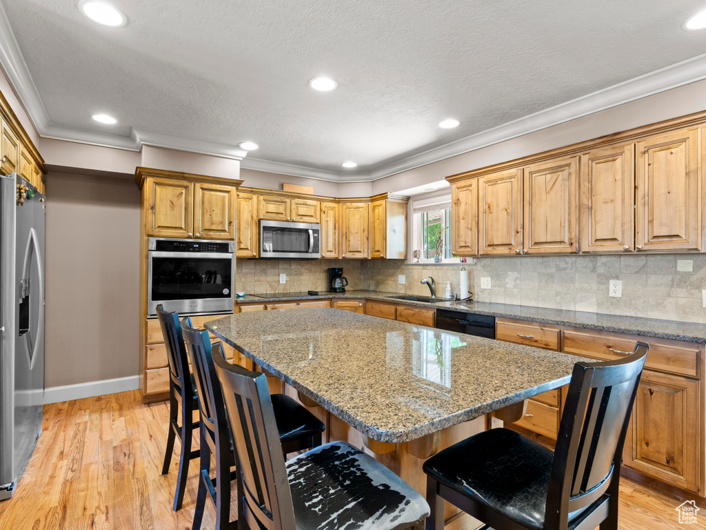 Kitchen featuring black appliances, crown molding, a kitchen bar, a kitchen island, and light wood-type flooring