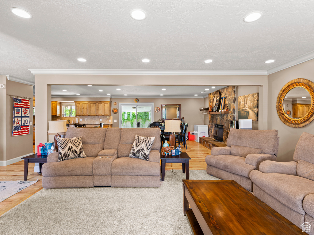Living area featuring ornamental molding, light wood-style floors, recessed lighting, and a stone fireplace